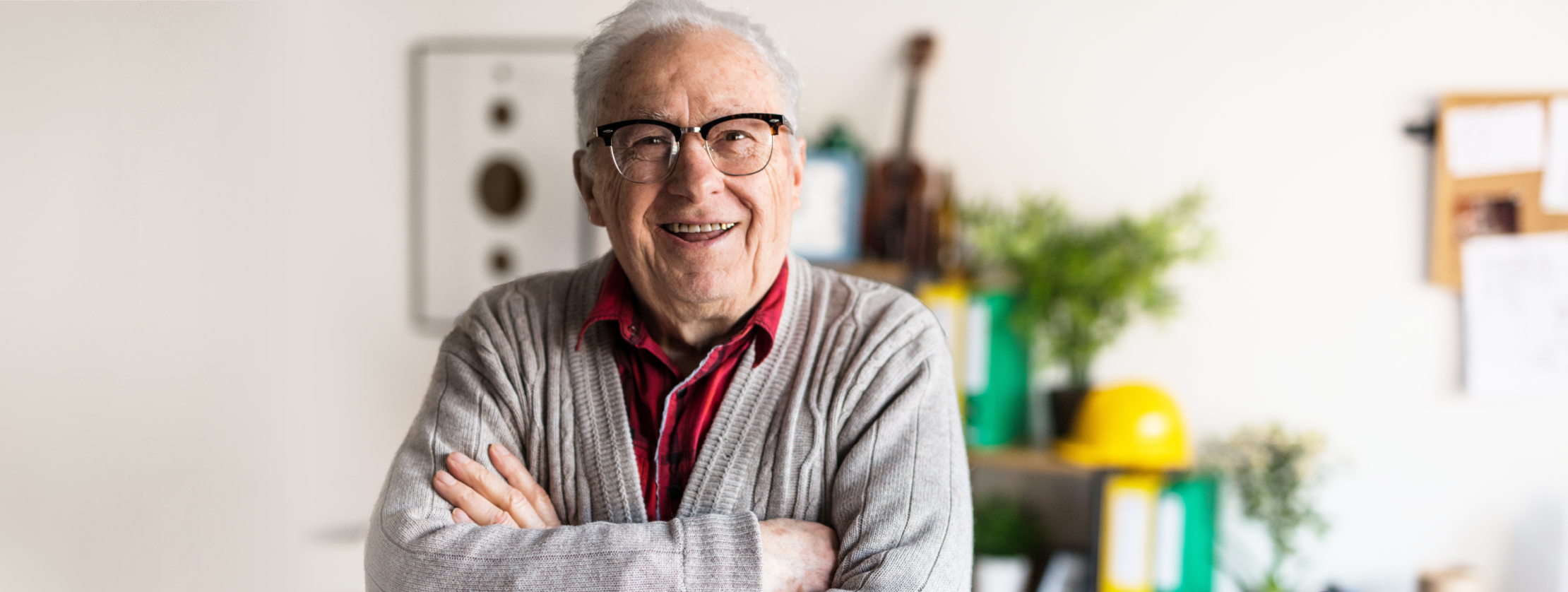 Ein Herr steht mit verschränkten Armen in einem Zimmer und lächelt in die Kamera.