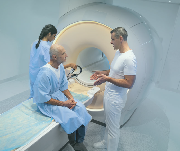 Ein Patient sitzt auf der Liegefläche eines MRT-Gerätes und unterhält sich mit einem Arzt.