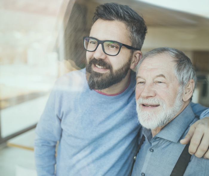 Ein junger Mann mit Brille steht neben einem älteren Herren und legt seinen Arm um dessen Schulter.