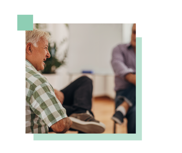 Ein älterer Herr ist in einem Gespräch mit einem anderen Mann im Hintergrund zu sehen.