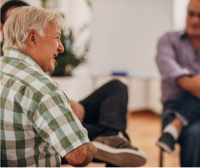 Ein älterer Herr ist in einem Gespräch mit einem anderen Mann im Hintergrund zu sehen.