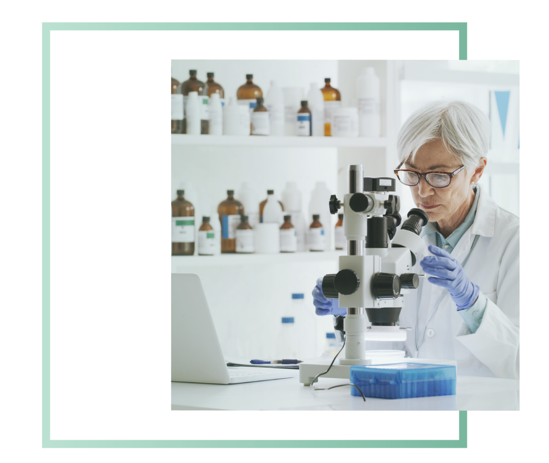 Eine Labormitarbeiterin mit Brille sitzt vor einem Mikroskop und untersucht eine Probe