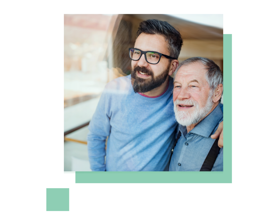 Ein junger Mann mit Brille steht neben einem älteren Herren und legt seinen Arm um dessen Schulter.