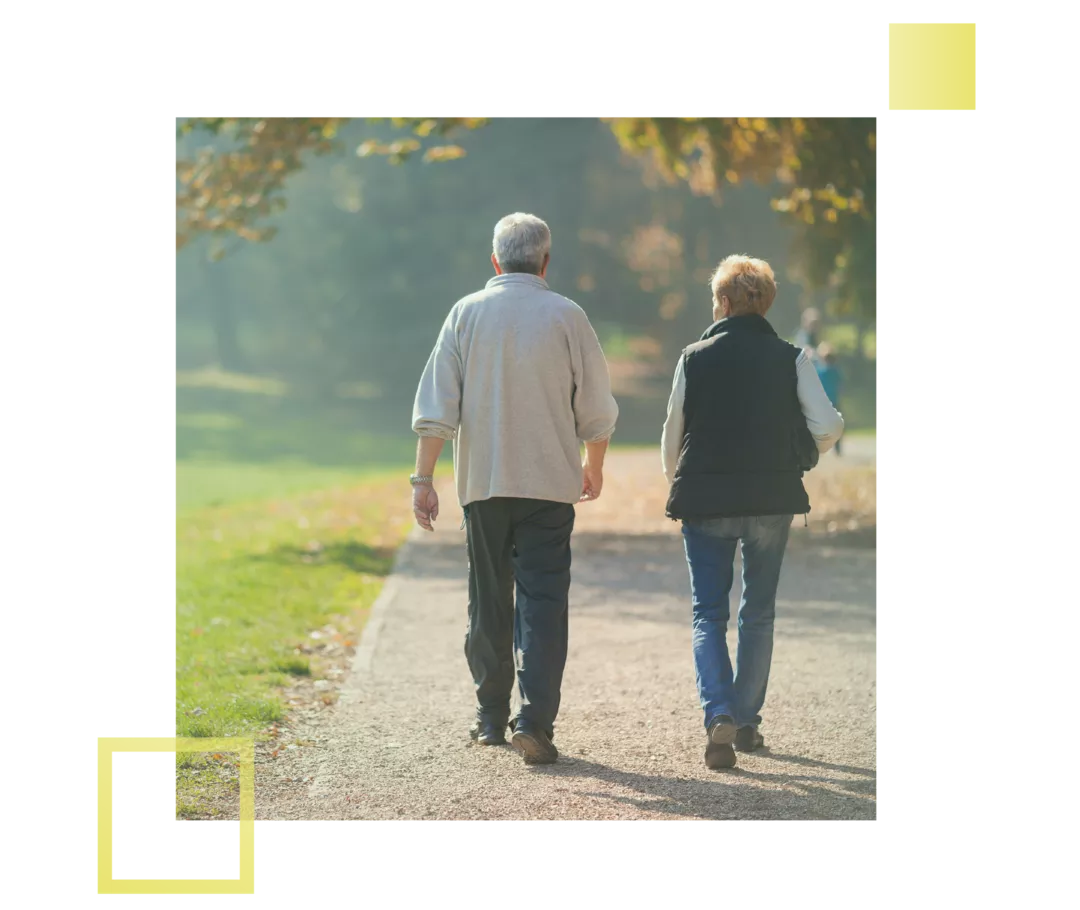 Ein älterer Mann und eine Frau gehen auf einem Waldweg spazieren.