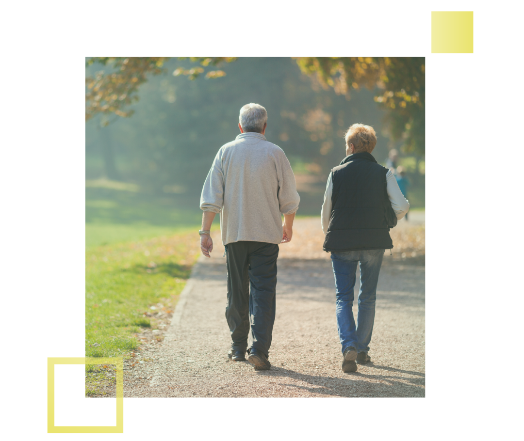 Leben mit fortgeschrittenem Prostatakarzinom: Ein älterer Mann und eine Frau gehen auf einem Waldweg spazieren. Ein älterer Mann und eine Frau gehen auf einem Waldweg spazieren.