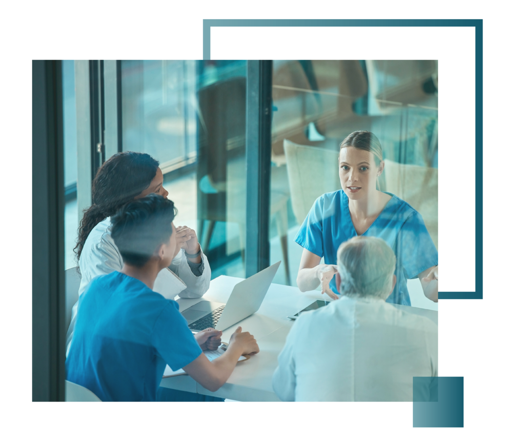 An einem Tisch sitzt eine Gruppe von Ärzt:innen und Schwestern. 