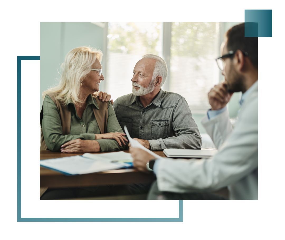 Ehepaar sitzt bei einem Beratungsgespräch einem Arzt gegenüber und schaut sich an.