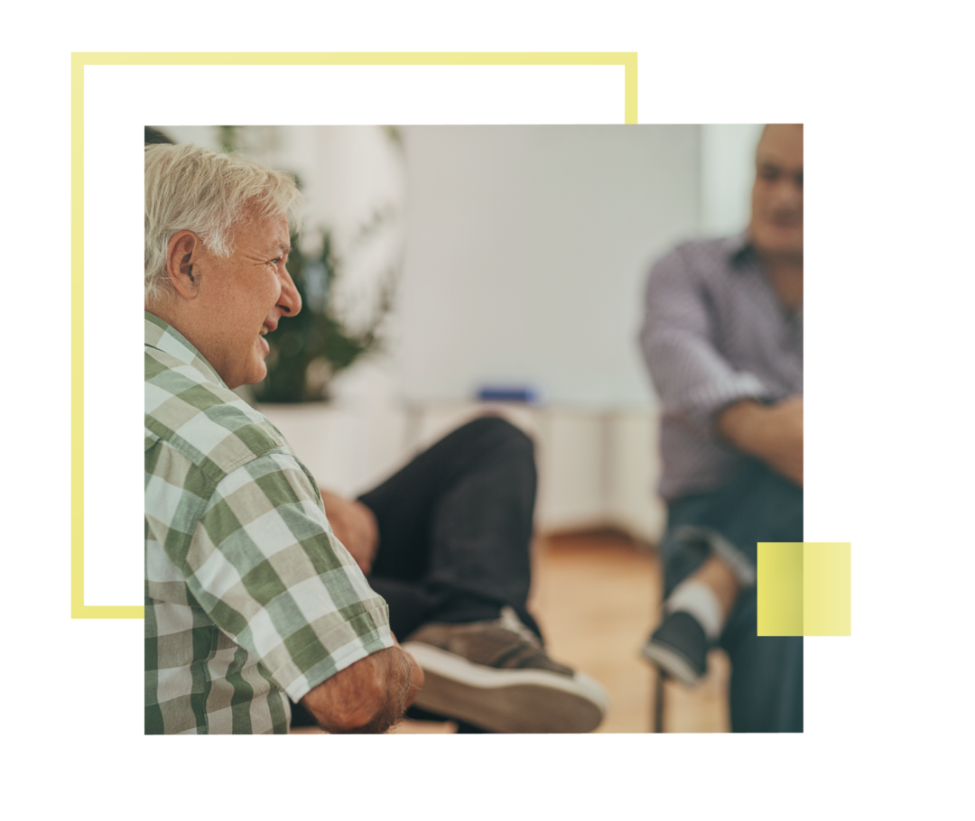 Älterer Herr in einem Gespräch mit einem anderen Mann im Hintergrund.