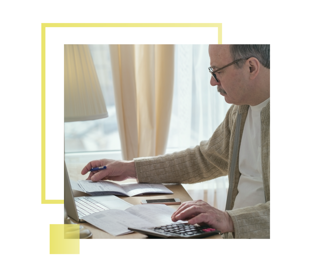 Mann mit Brille schaut Dokumente durch und rechnet seine Finanzen mit dem Taschenrechner.